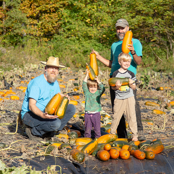 Two adults and two children in a squash patch.