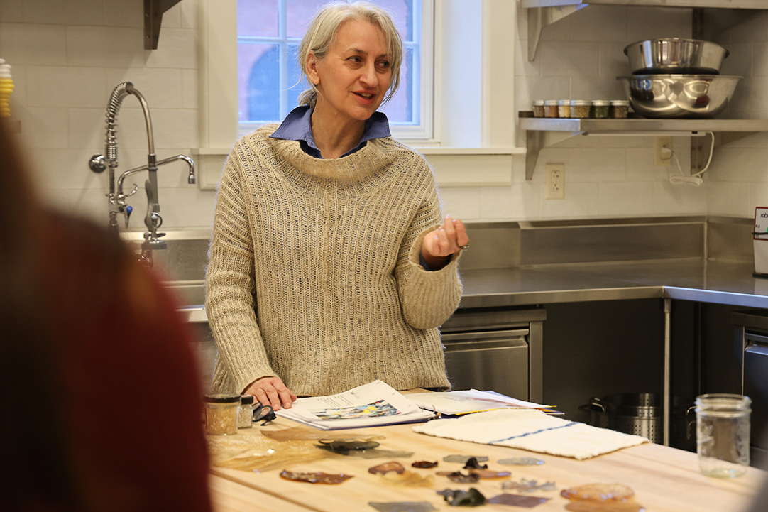 A woman in a sweater talks to a group in an industrial kitchen