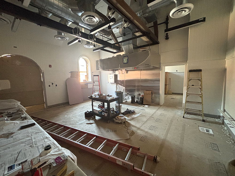 a very under construction commercial kitchen, with ladders, a movable work table, ceiling venting system, and floor covered with protective heavy duty paper.