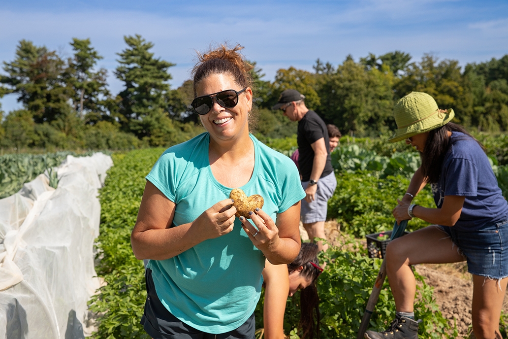 A woman smiles while holding a heart shaped potato in a potato field