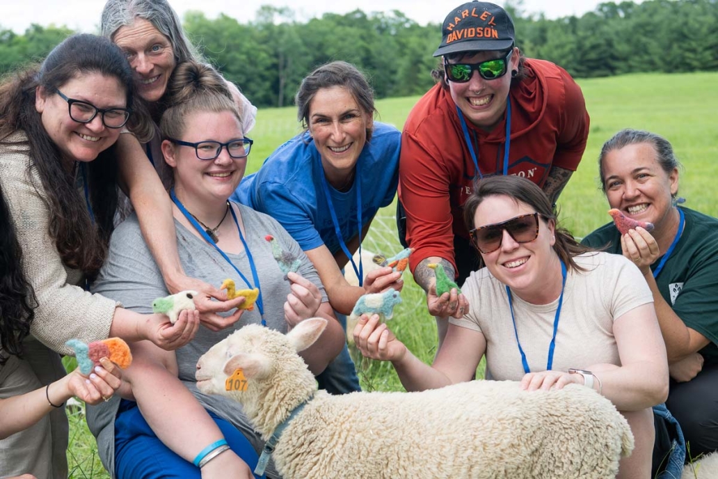 A group of people smiling, gathered around a lamb. They are holding colorful felted figurines.
