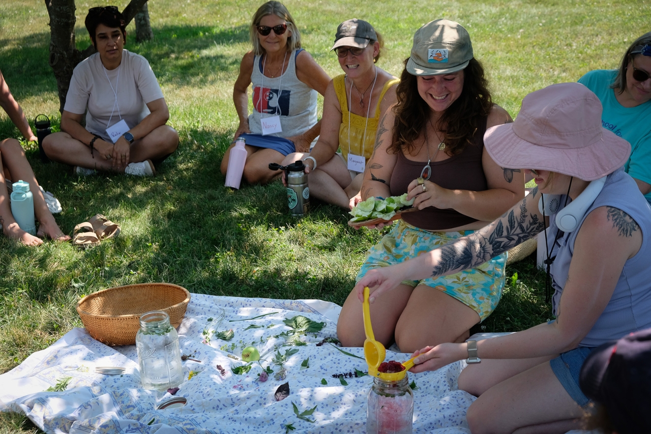 A group of women gather around a blanket making tea during a workshop