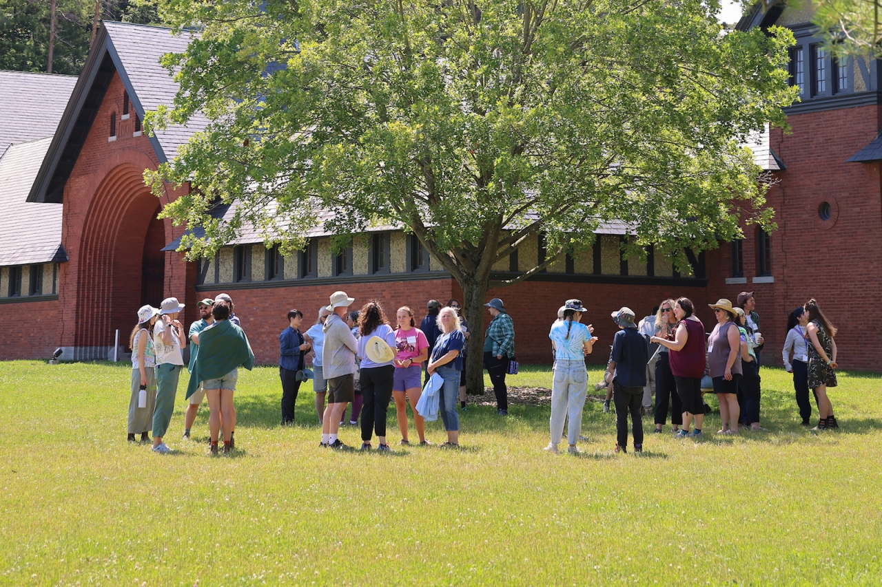 Thirty people stand in a circle in front of a large brick building
