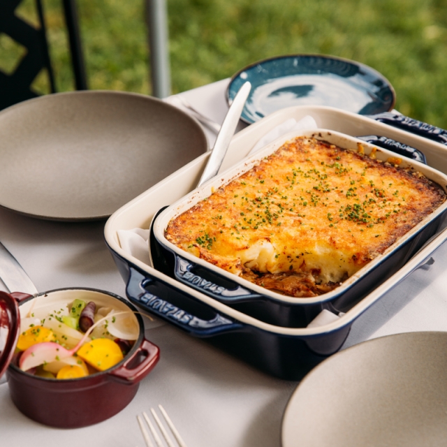 A casserole dish with Shepherd's Pis sits on an outdoor dining table, set for dinner.