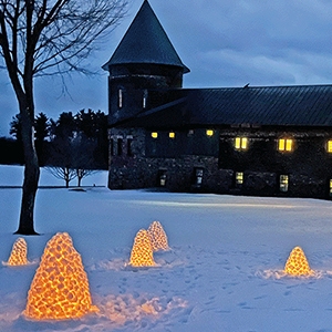 Small illuminated igloos at dusk in front of a large barn in wintertime