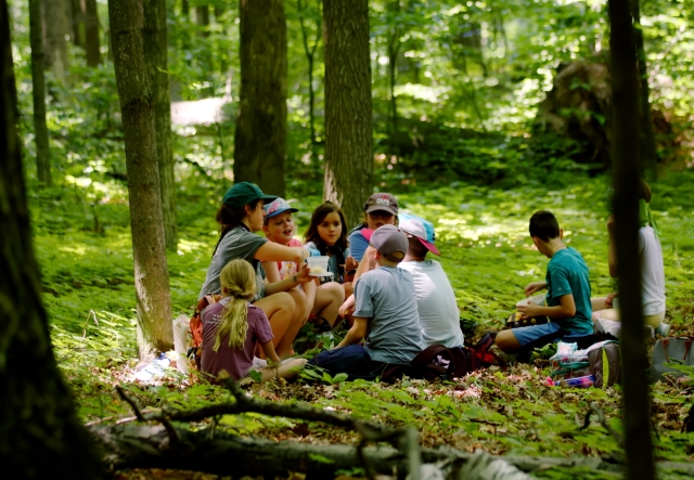 camp counselor surrounded by students sitting in the woods