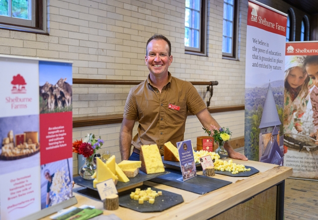 Man in short-sleeved shirt behind a table showcasing various cheeses