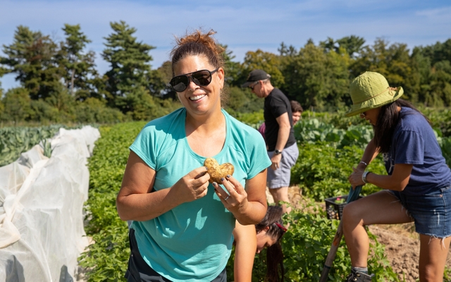 A woman smiles while holding a heart shaped potato in a potato field