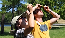 Two adults smile while holding green leaves up to the sunlight