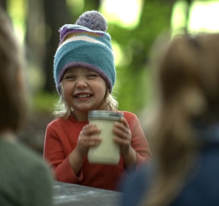 A child smiles as she shakes a jar of cream, turning it to butter.